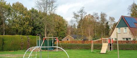 A playground with swings and a slide, surrounded by a well-maintained lawn and a house with solar panels.