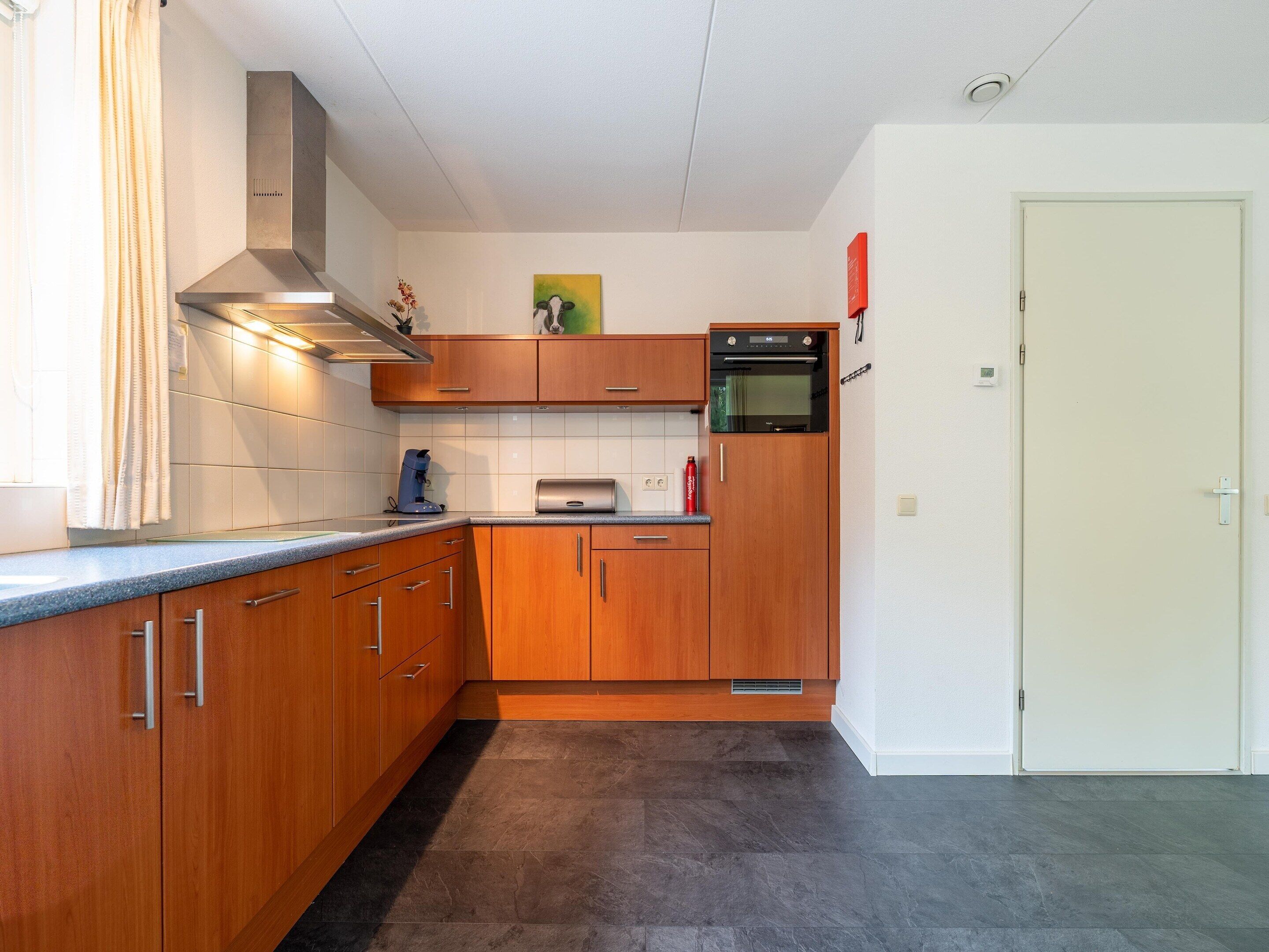 A compact kitchen with wooden cabinets, a built-in oven, and a coffee maker.