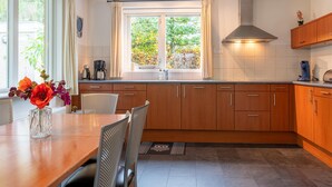 Een moderne keuken met houten kastjes, een eettafel en een raam met uitzicht op bomen.