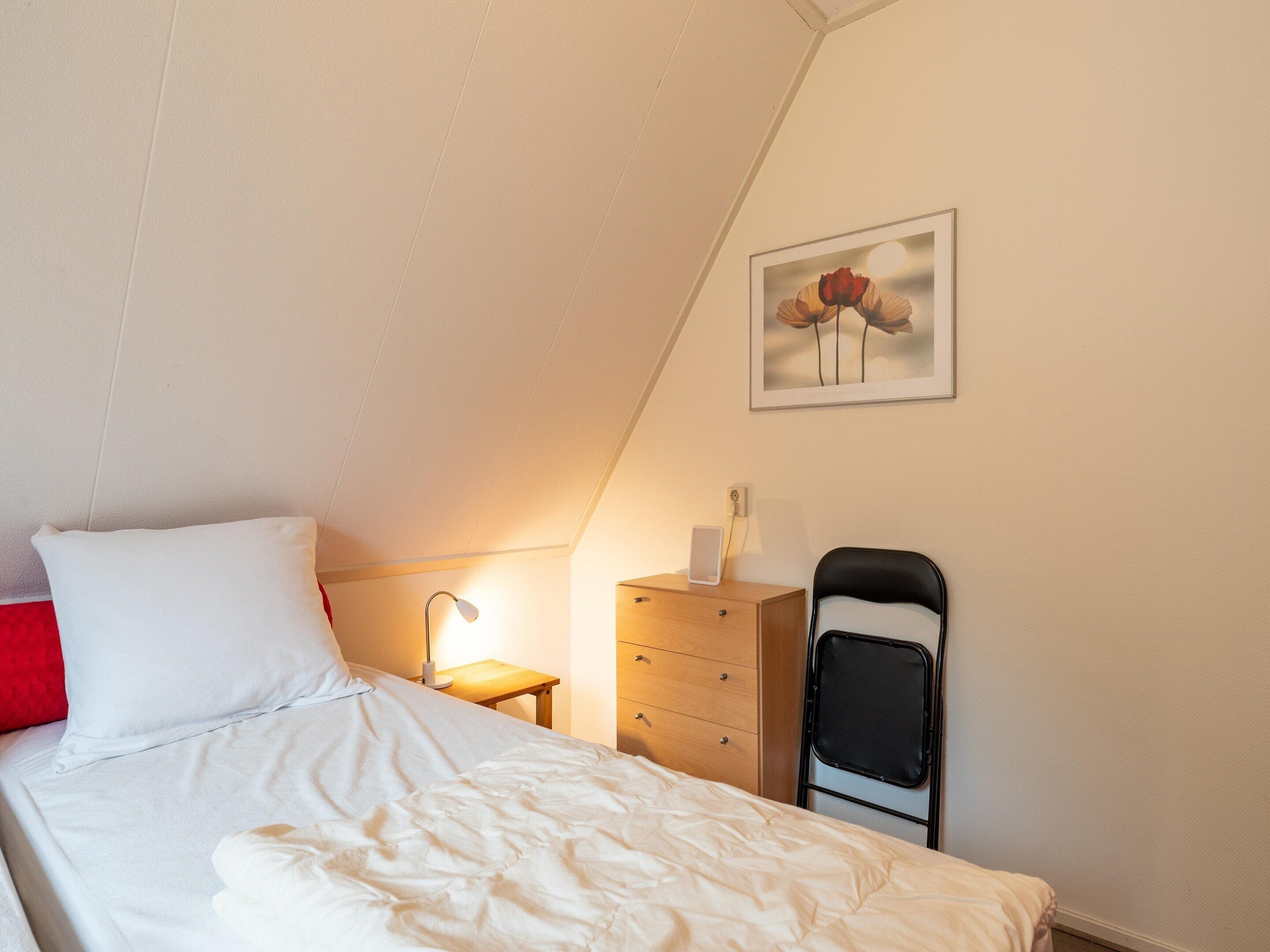 A bedroom with a bed, a nightstand, a dresser, a chair, and a framed picture on the wall.