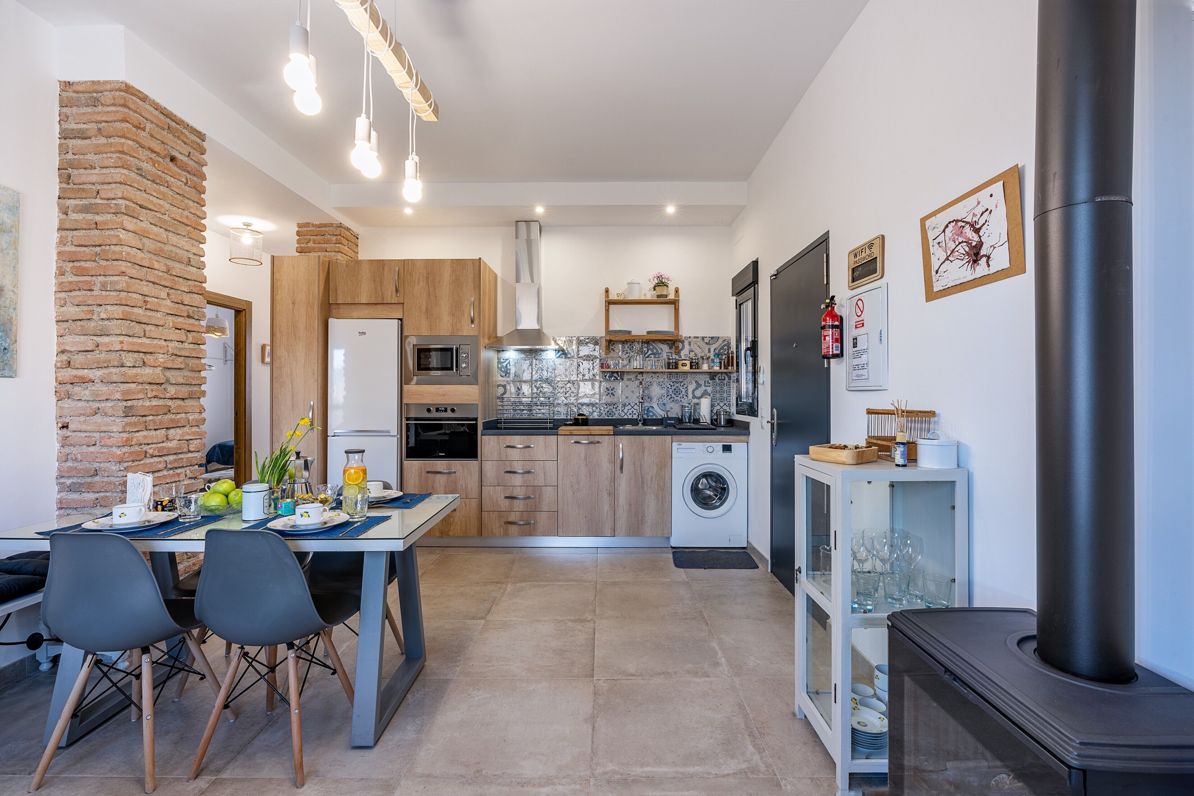 Una cocina moderna con pared de ladrillo, armarios de madera, horno empotrado, microondas y lavadora.