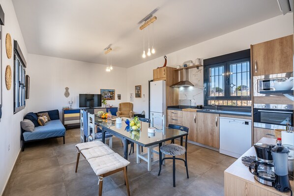 A modern kitchen with a dining area, a sofa, and a TV.