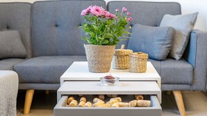 Un canapé gris, une table basse blanche avec un pot de plante, des paniers en osier et un porte-bouteille à vin.