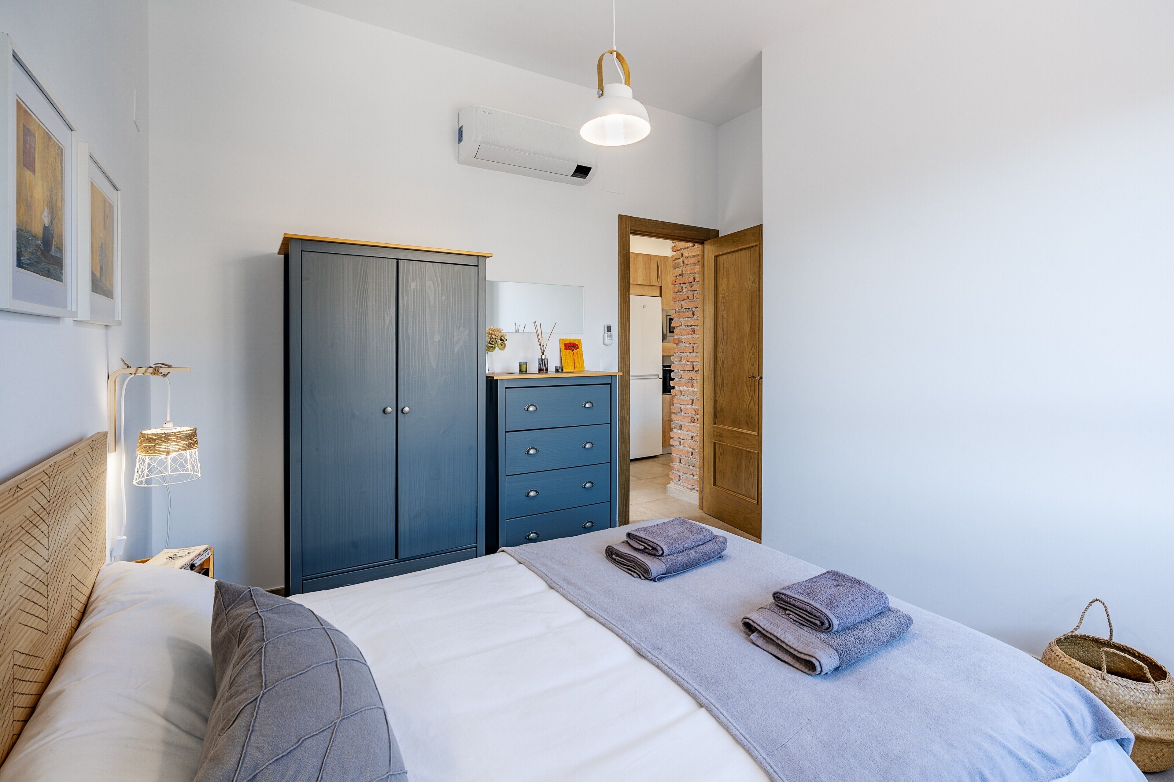 A bedroom with a bed, a wardrobe, a hanging lamp, and a door leading to a bathroom.