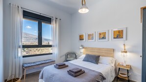 Une chambre à coucher avec un grand lit, un banc, une table de chevet, une lampe et des œuvres d’art encadrées accrochées au mur.