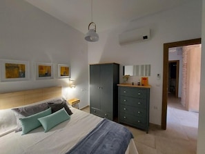 A bedroom with a bed, a wardrobe, a nightstand, and a wall-mounted lamp.