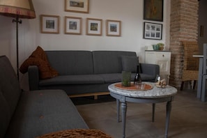A living room with a grey sofa, a round table with a vase and a glass, and framed pictures on the wall.