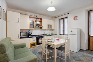 A compact kitchen with a dining table, chairs, a sofa, and a refrigerator.