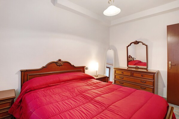 A bedroom with a wooden bed, a dresser, a mirror, and a door.
