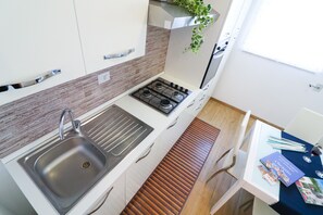 A compact kitchen with a stainless steel sink, a gas stove, and a wooden slatted bench.