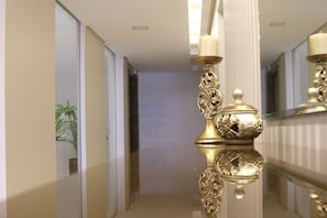 En elegant hal med et spejlblankt gulv, en dekorativ guldfarvet lampe og en potteplante.