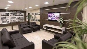 A modern hotel lobby with black leather sofas, a TV on the wall, and a display of the hotel's history. - Tri Hotel Xanxerê (Xanxere)