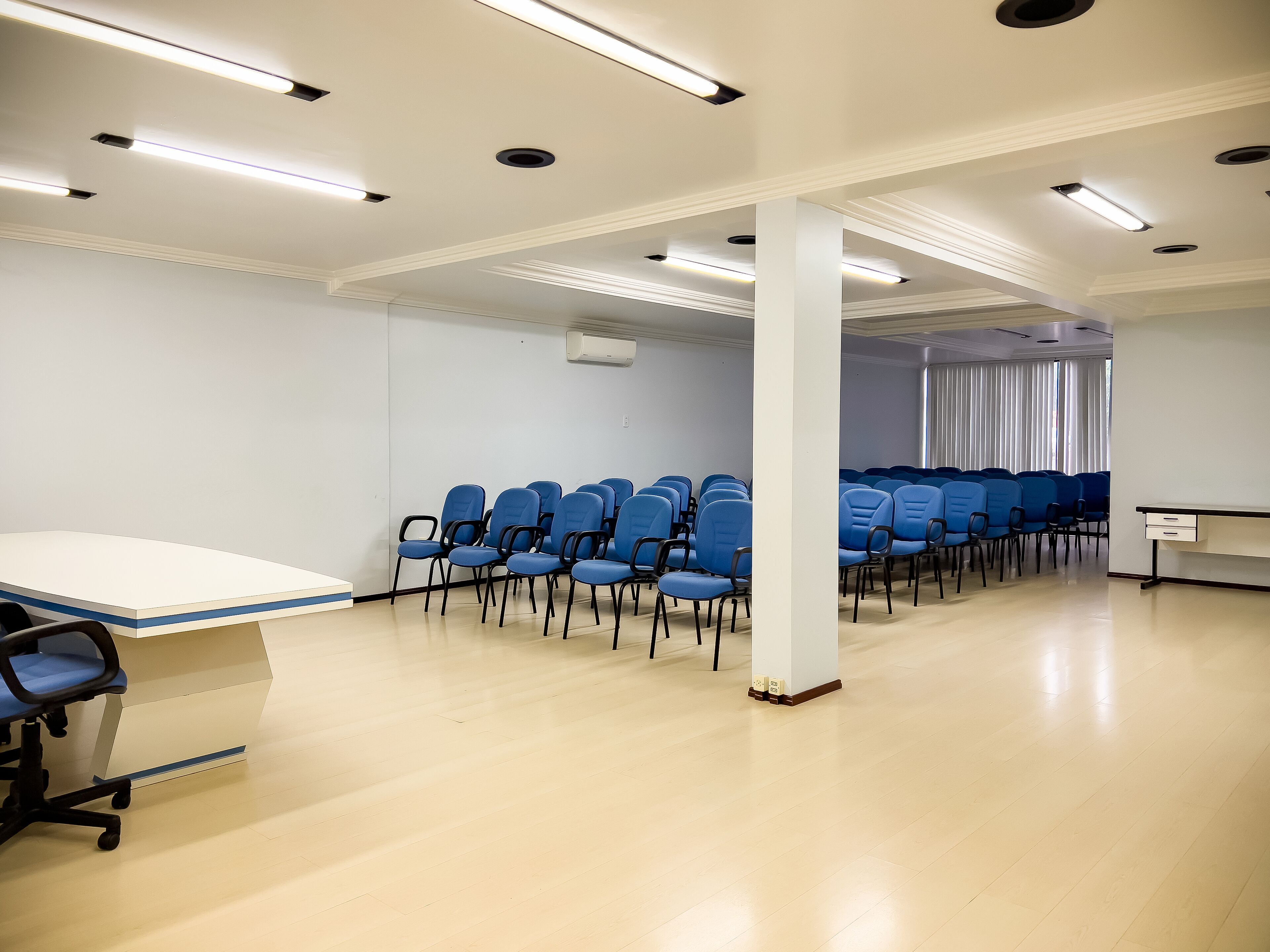 A conference room with rows of blue chairs, a white table, and recessed ceiling lighting.