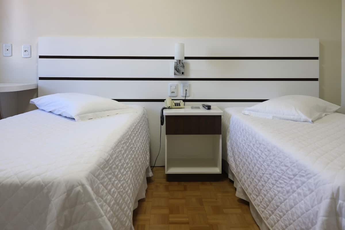 Ein Hotelzimmer mit zwei Einzelbetten, einem Nachttisch mit Lampe, einem Telefon und einer Steckdose.