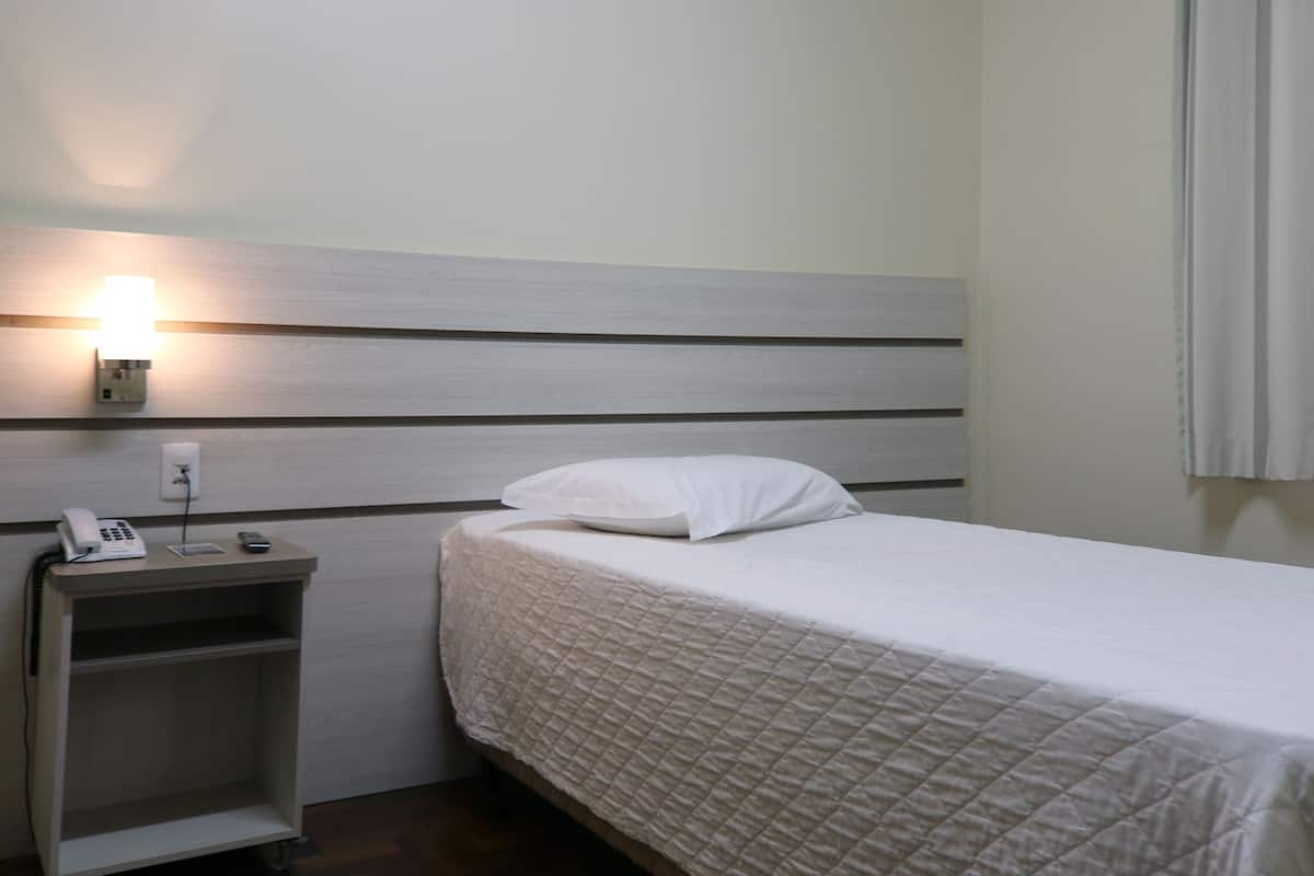 Ein ordentlich bezogenes Bett mit einer gesteppten weißen Daunendecke, einer Nachttischlampe und einem Telefon auf einem Holznachttisch.