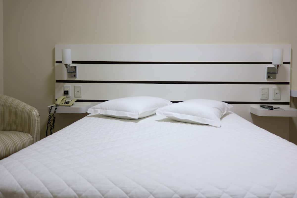 Ein Hotelzimmer mit einem Bett, zwei Kissen, einem Nachttisch mit Telefon und einem Sessel.