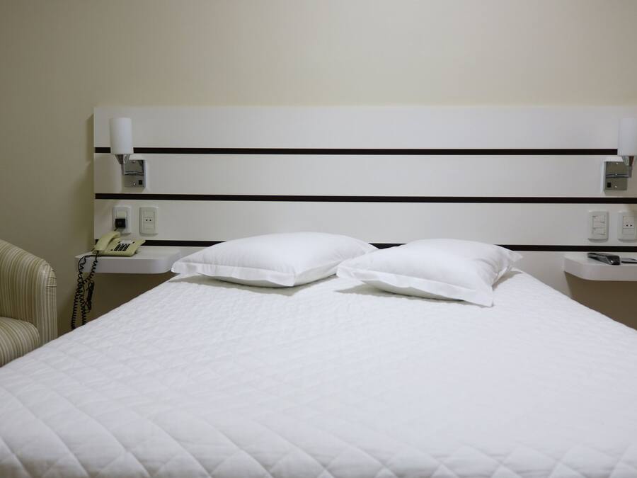 A hotel room with a bed, two pillows, a bedside table with a phone, and a chair.