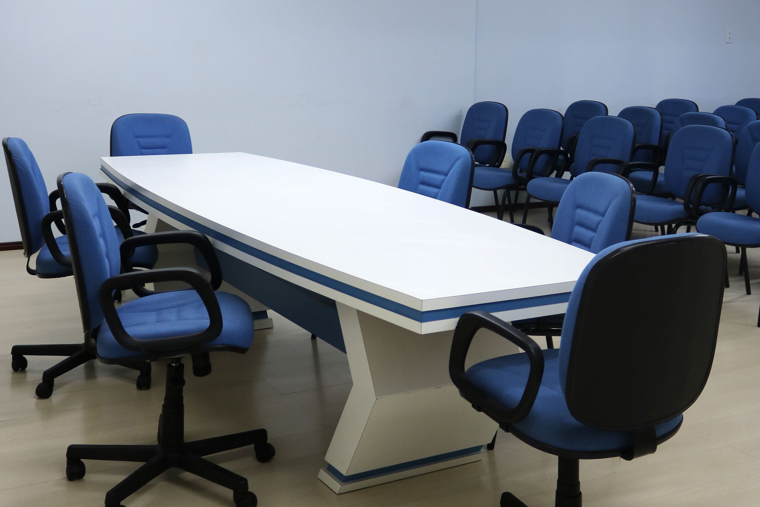 A conference room with a long table and multiple blue chairs.