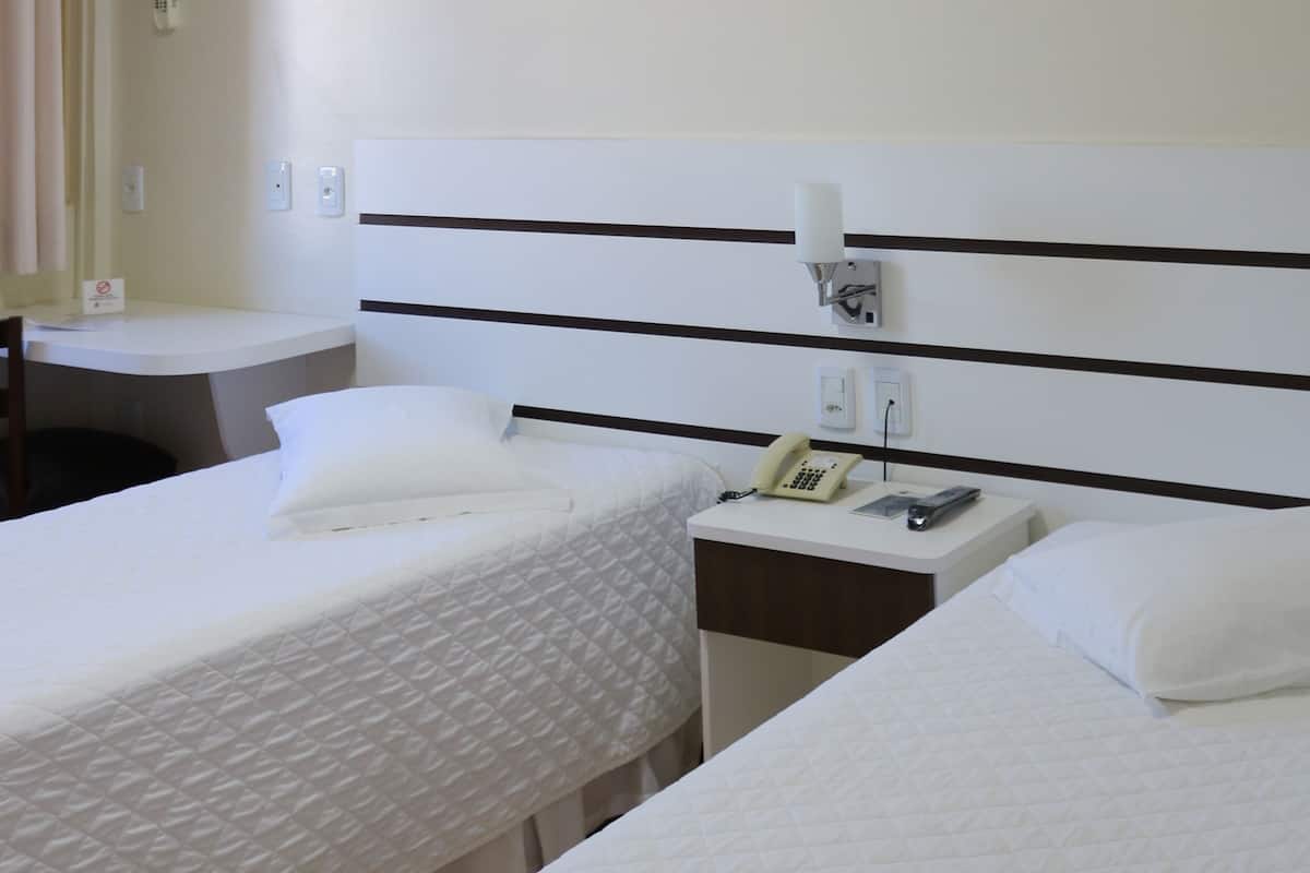 Ein Hotelzimmer mit zwei Einzelbetten, einem Nachttisch mit Telefon und Lampe sowie einem kleinen Schreibtisch mit Stuhl.