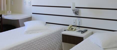 Habitación de hotel con dos camas individuales, una mesita de noche con teléfono y lámpara, y un escritorio pequeño con silla.