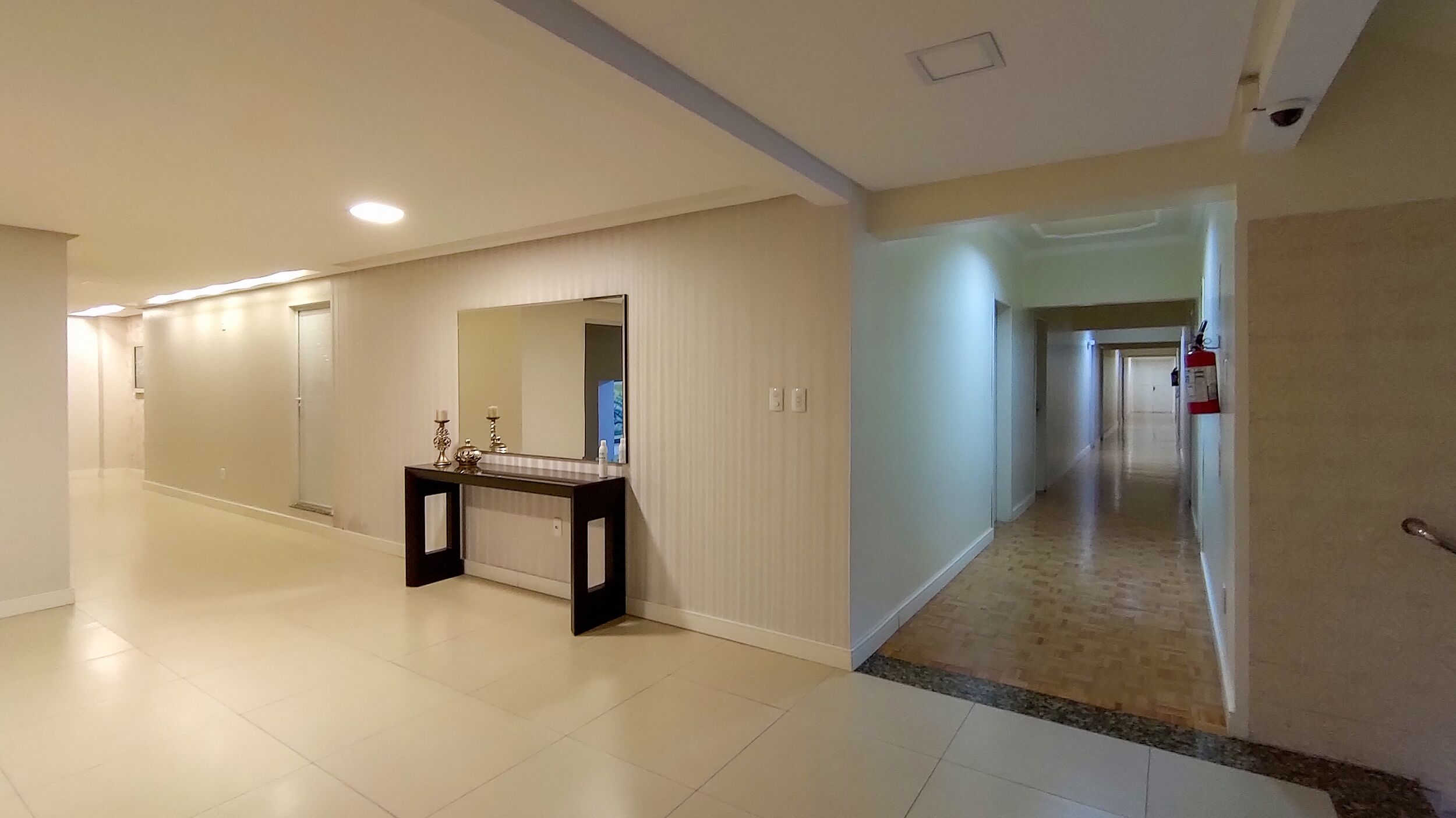 A spacious hallway with a vanity area featuring a mirror, a small table, and a wall-mounted fire extinguisher.
