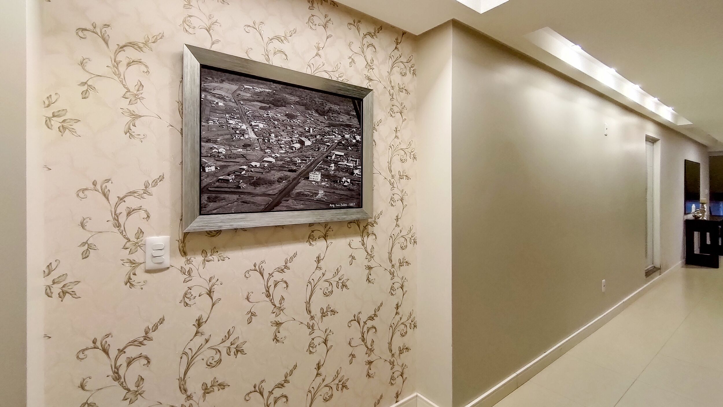Ein Flur mit einem schwarzen und weißen Foto in einem Rahmen an der Wand, blumigem Wandpapier und einem klaren, modernen Design.