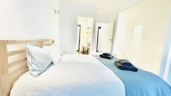 A bedroom with a wooden headboard, a large bed with white bedding, a blue blanket, and a pair of slippers on the floor. - Townhouse Bombarda (Lagos)