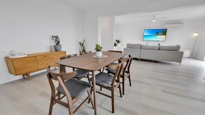 Ein modernes Wohnzimmer mit Essbereich, ausgestattet mit einem Holzesstisch und sechs Stühlen, einem grauen Sofa und einem Flachbildfernseher an der Wand.