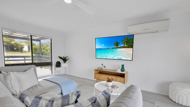 Ein modernes Wohnzimmer mit großem Flachbildfernseher, einer Couch mit gestreiften Kissen, einem Couchtisch und einer Holzkommode.
