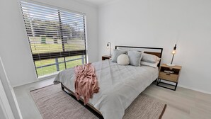 Ein Schlafzimmer mit Bett, Nachttischen, einem Fenster mit Jalousien und Blick ins Freie.