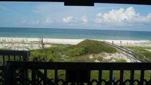 A beach view with a wooden deck and a sandy path leading to the water.