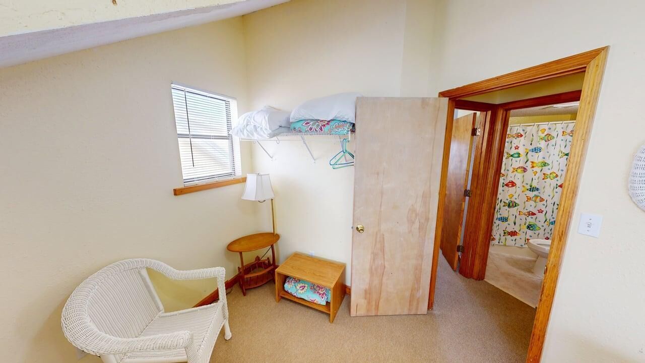 A compact room with a bed, a small table, a chair, a window, and a door leading to a bathroom.