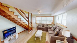A living room with a wooden staircase, a television, a sofa set, and a lamp.