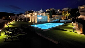 Zona de piscina con muro de piedra, sillas de descanso y un patio bien iluminado.
