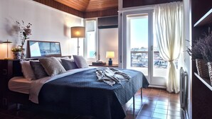 Un dormitorio con una cama grande, una mesita de noche, una lámpara, una ventana con cortinas y vistas a edificios.