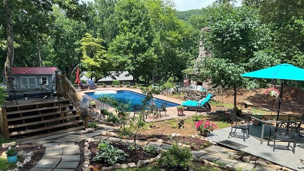 A backyard with a swimming pool, a wooden deck, and a patio area with outdoor furniture.