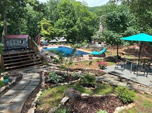 A backyard with a swimming pool, a wooden deck, and a patio area with outdoor furniture.