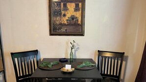 A dining table with two chairs, a framed painting on the wall, and a vase with flowers on the table.