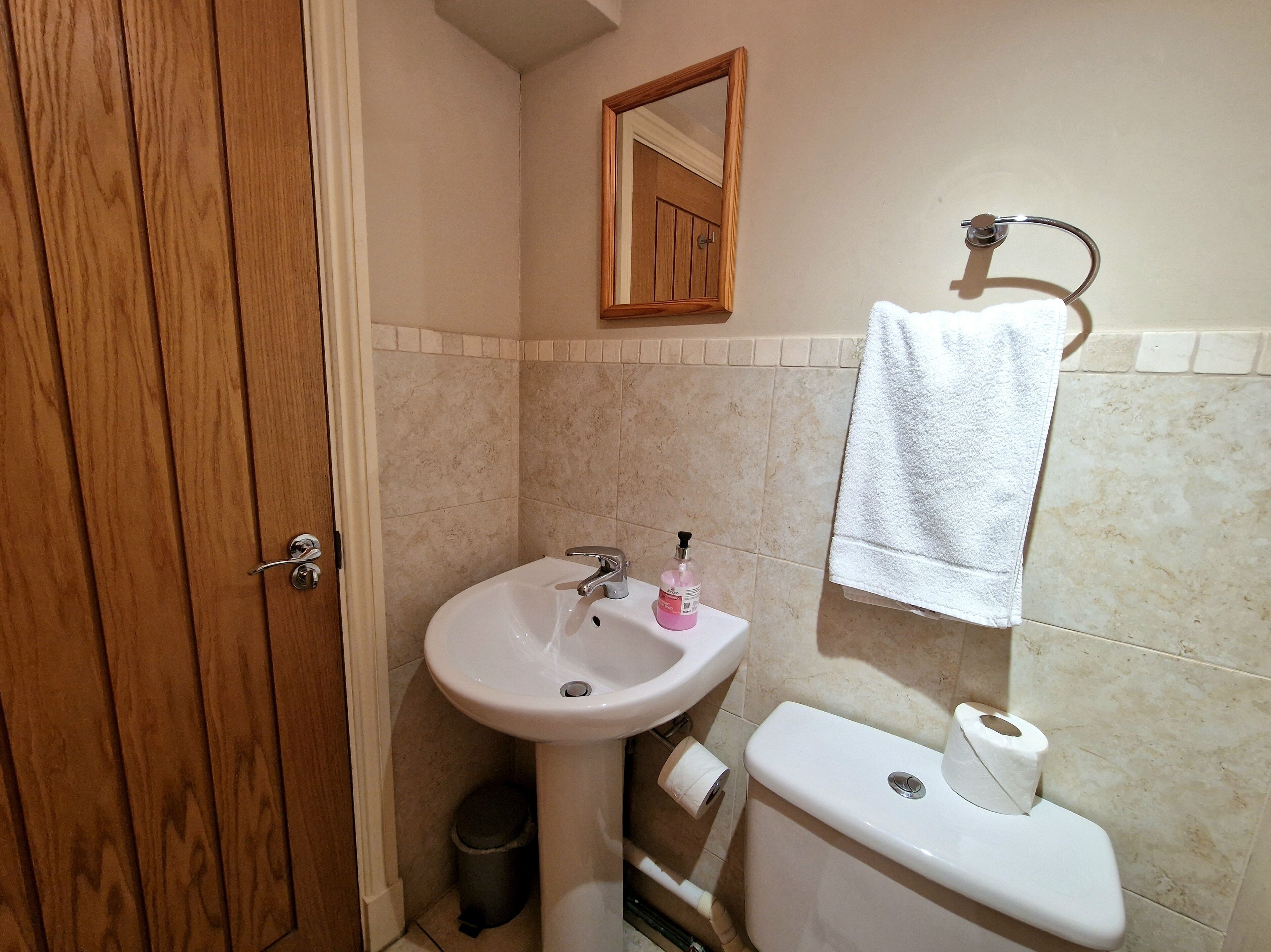 A bathroom with a wooden door, a white sink, a toilet, and a towel hanging on a rack.