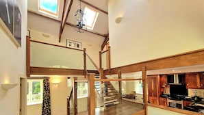 A spacious loft-style apartment with a wooden staircase, a kitchen area, and a large window providing natural light. - Clifton Cottage at Lovelady Shield (Alston)