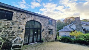 A stone building with a large arched entrance, a small window, and a bench outside. - Clifton Cottage at Lovelady Shield (Alston)