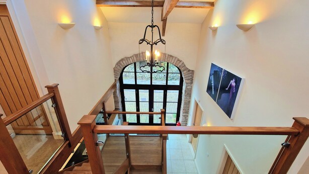 A wooden staircase with glass railings leading to a landing with a stone archway and a large window. - Clifton Cottage at Lovelady Shield (Alston)