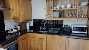 Een keuken met houten kastjes, een zwart aanrecht, een spoelbak, een kookplaat en een magnetron.