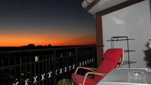 A balcony with a red chair and a table, overlooking a sunset. - Comfortable apartment in nature (FREE PARKING)-just a stone's throw from the park (Castel di Leva)