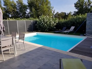 A rectangular swimming pool with a tiled deck, surrounded by a low fence and lush greenery.