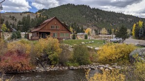 A rustic cabin with a deck, surrounded by autumn foliage and a mountain backdrop. - Fabulous 5 BR Vacation Home on the Taylor River (Almont)