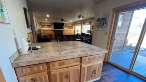 A spacious kitchen with a large island, wooden cabinetry, and a sliding glass door leading to an outdoor area. - Fabulous 5 BR Vacation Home on the Taylor River (Almont)