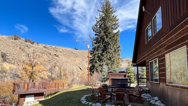 A wooden cabin with a deck, a barbecue area, and a view of a forested hillside. - Fabulous 5 BR Vacation Home on the Taylor River (Almont)
