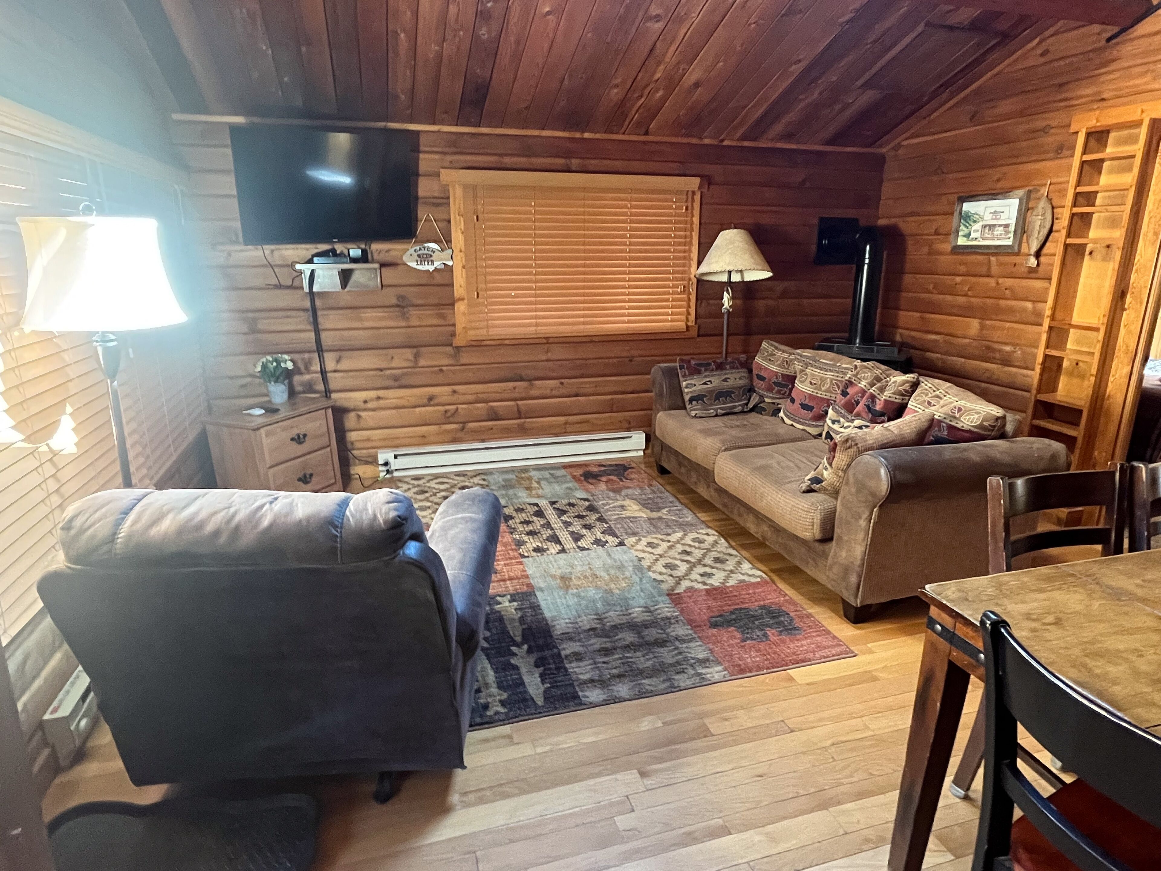 A cozy log cabin interior with a sofa, a dining table, and a television.