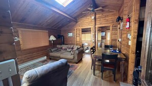 Interior acogedor de una cabaña de madera con comedor, sofá y ventilador de techo.